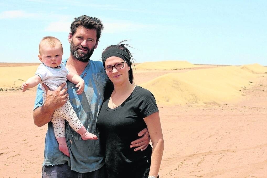 Bradd and Mykala Vermeersch with their eight-month-old son George in front of grain that was stored in silo bags before they melted off in the fire.