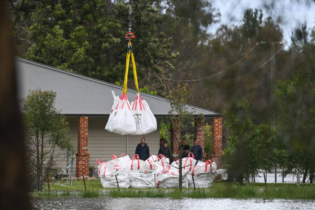 Property owners watch on as a helicopter drops several loads of sandbags prepared at Gateway Lakes into their yard to prevent rising floodwaters from reaching the home after already swamping the 140-acre cattle farm in Wodonga on Wednesday. Pictures by Mark Jesser
